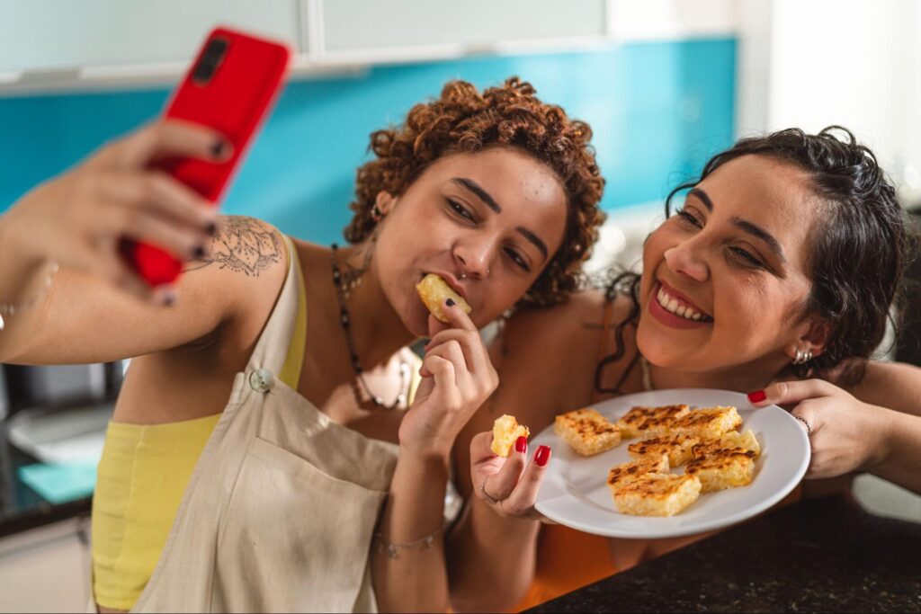 Duas pessoas tirando fotos de um celular experimentando um prato de comida.